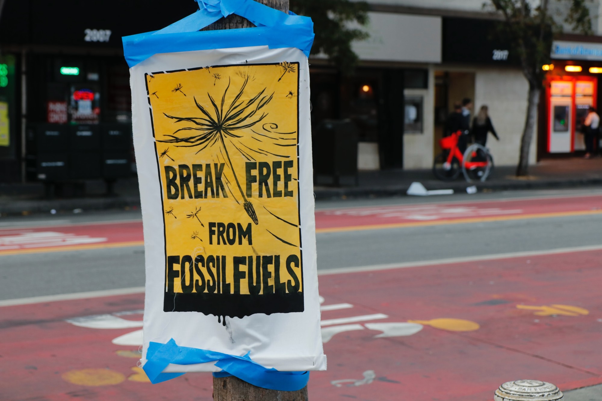 A yellow and white poster from a climate action poster is taped to a pole on a street in San Francisco. The sign says break free from fossil fuels.